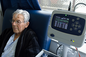 An image of an elderly man sitting next to a medical monitor