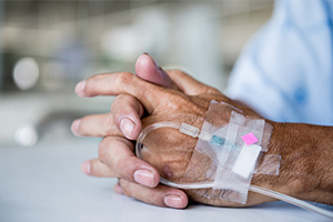 An image of hands folded together with an IV inserted